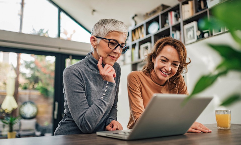Two casual women looking at laptop indoors, portrait.