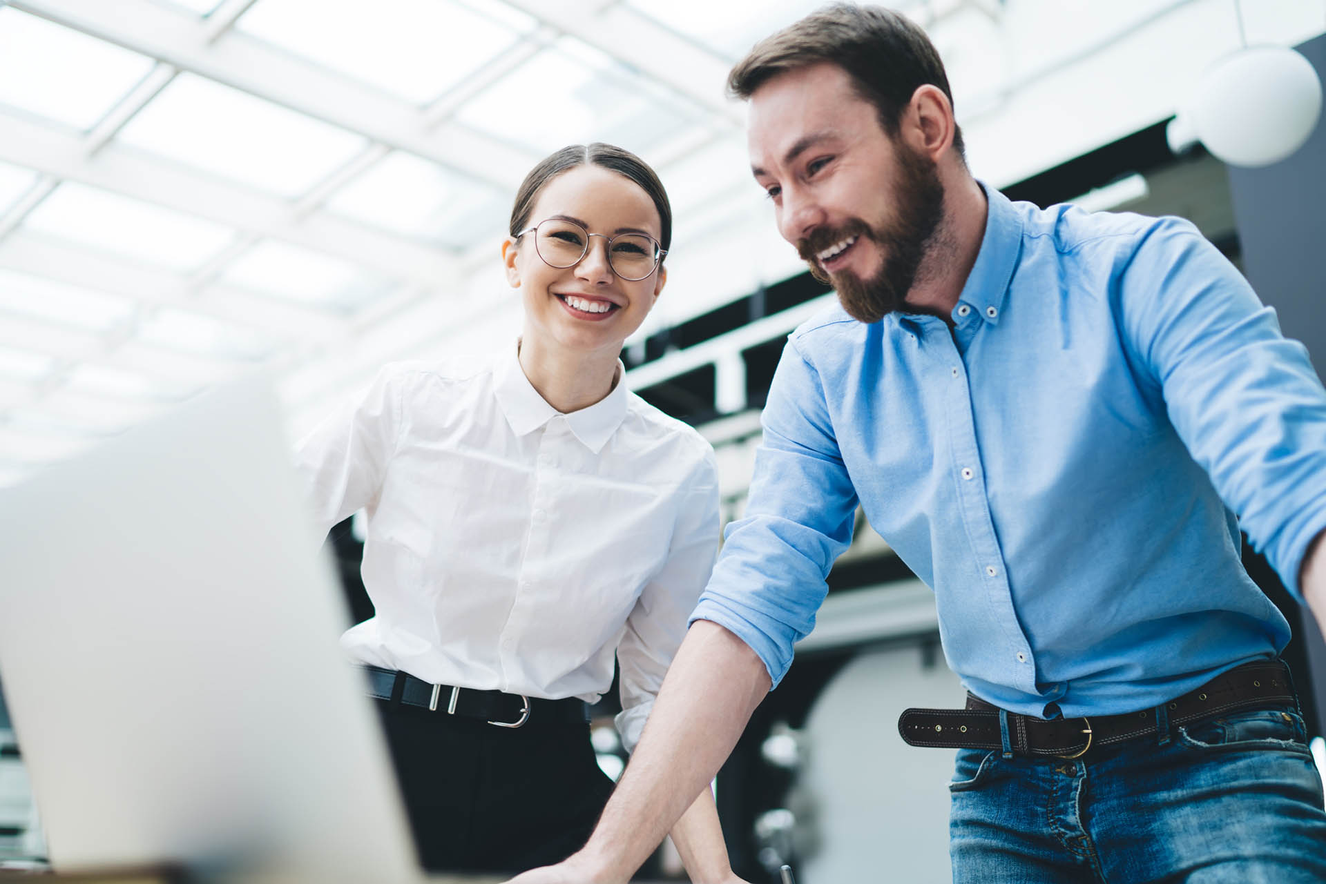 Adult colleagues laughing while discussing project at laptop in office